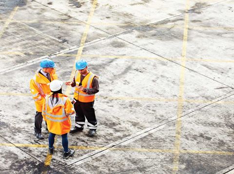 three people standing at the construction side wearing protective personal equipment.